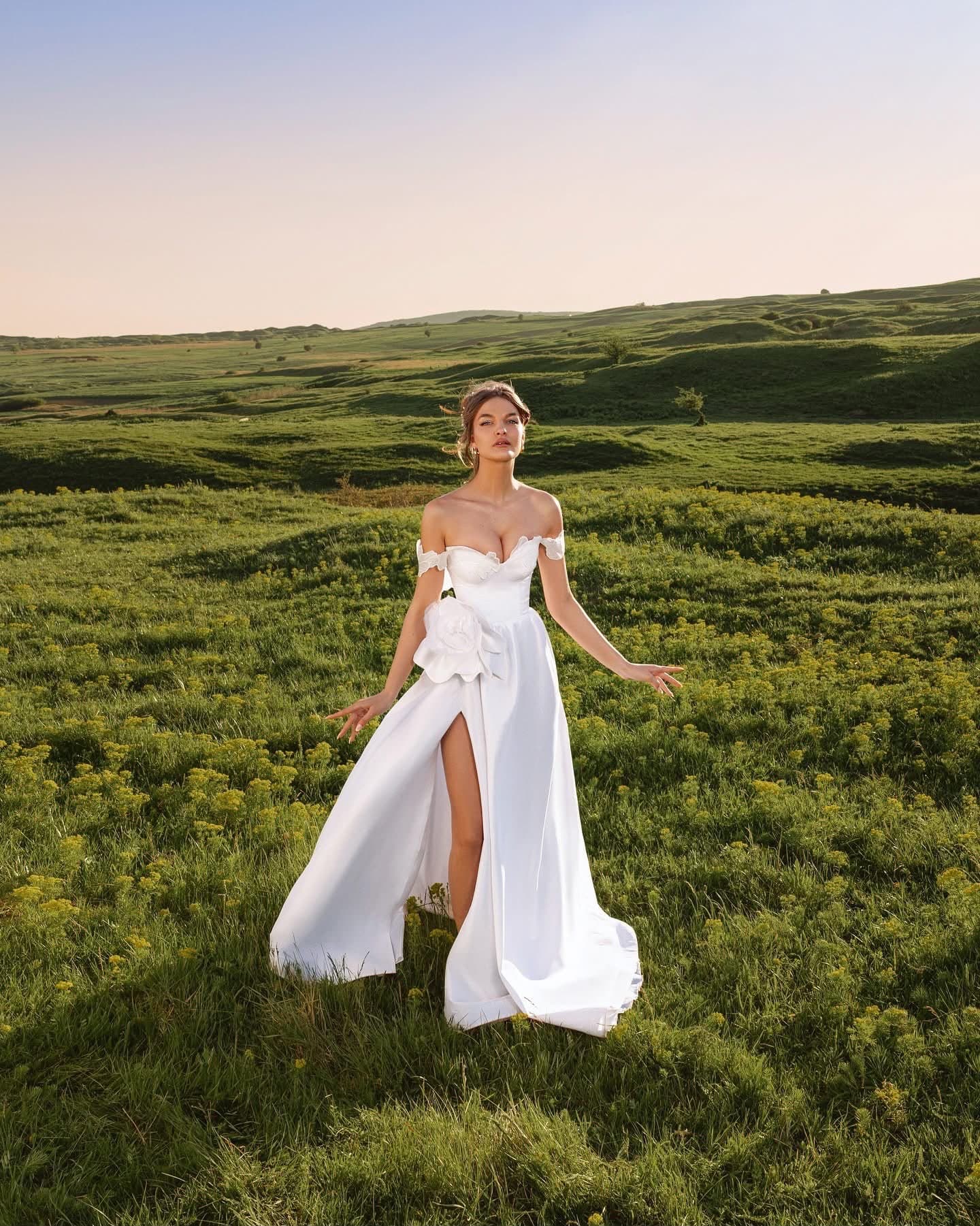 Bride in the Rose Fendue Gown, full length, on a green hillside