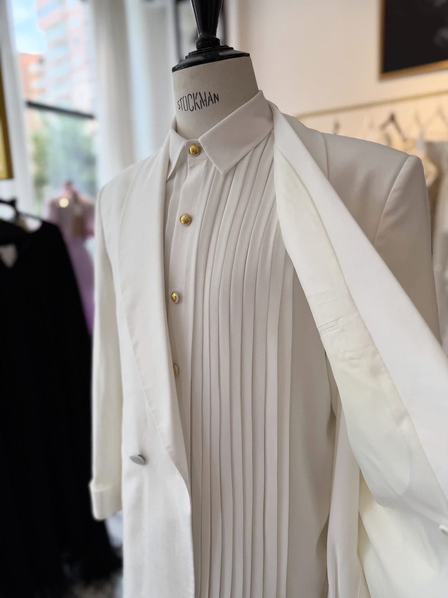 White tuxedo jacket and pleated shirt on a mannequin in the atelier