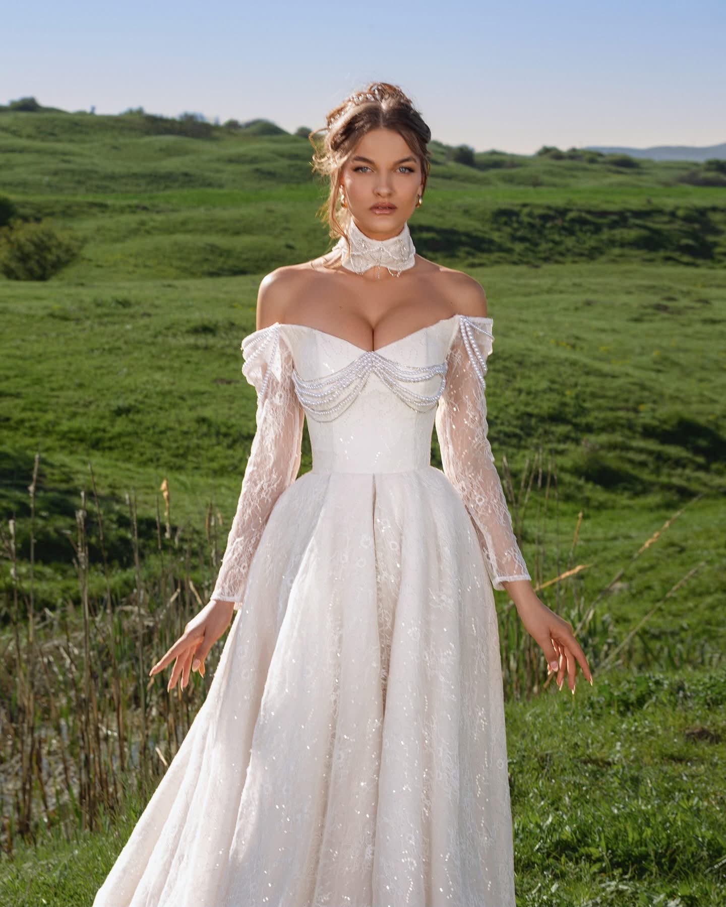 Bride in the Manches Illusion Gown with sheer beaded sleeves and choker, close view on a hillside
