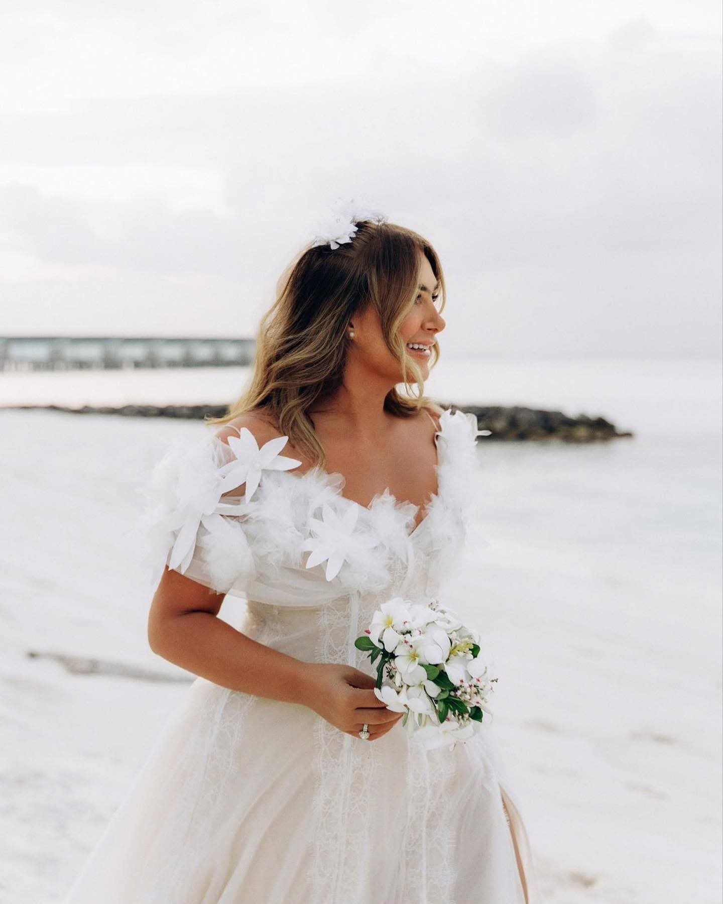 Close view of the flower sleeves of the Voile Fleuri Gown, bride holding a bouquet by the sea