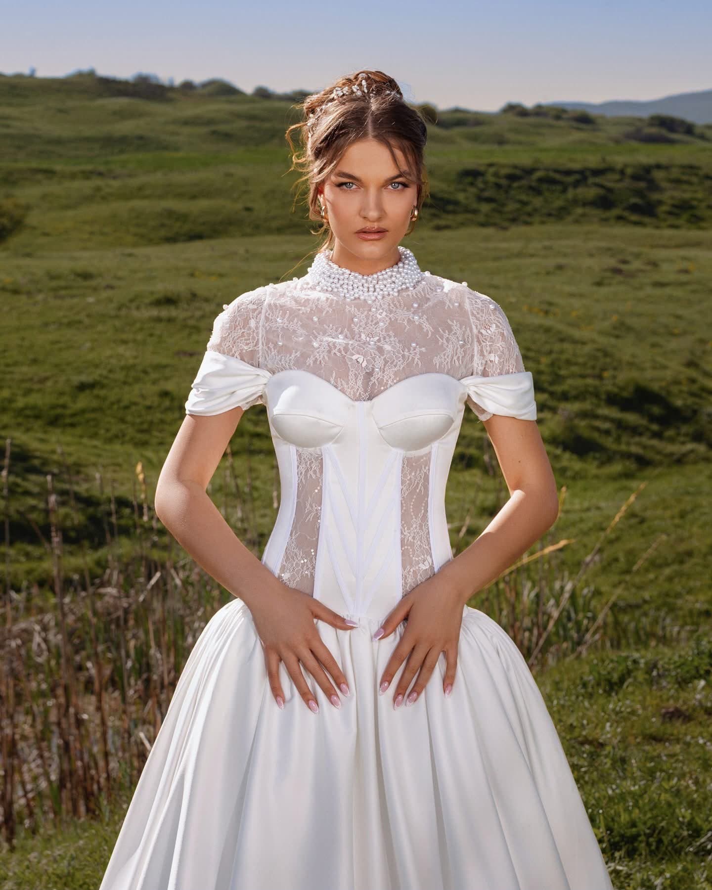 Bride in the Col Montant Gown with high lace collar, draped sleeves and full satin skirt, close view on a hillside