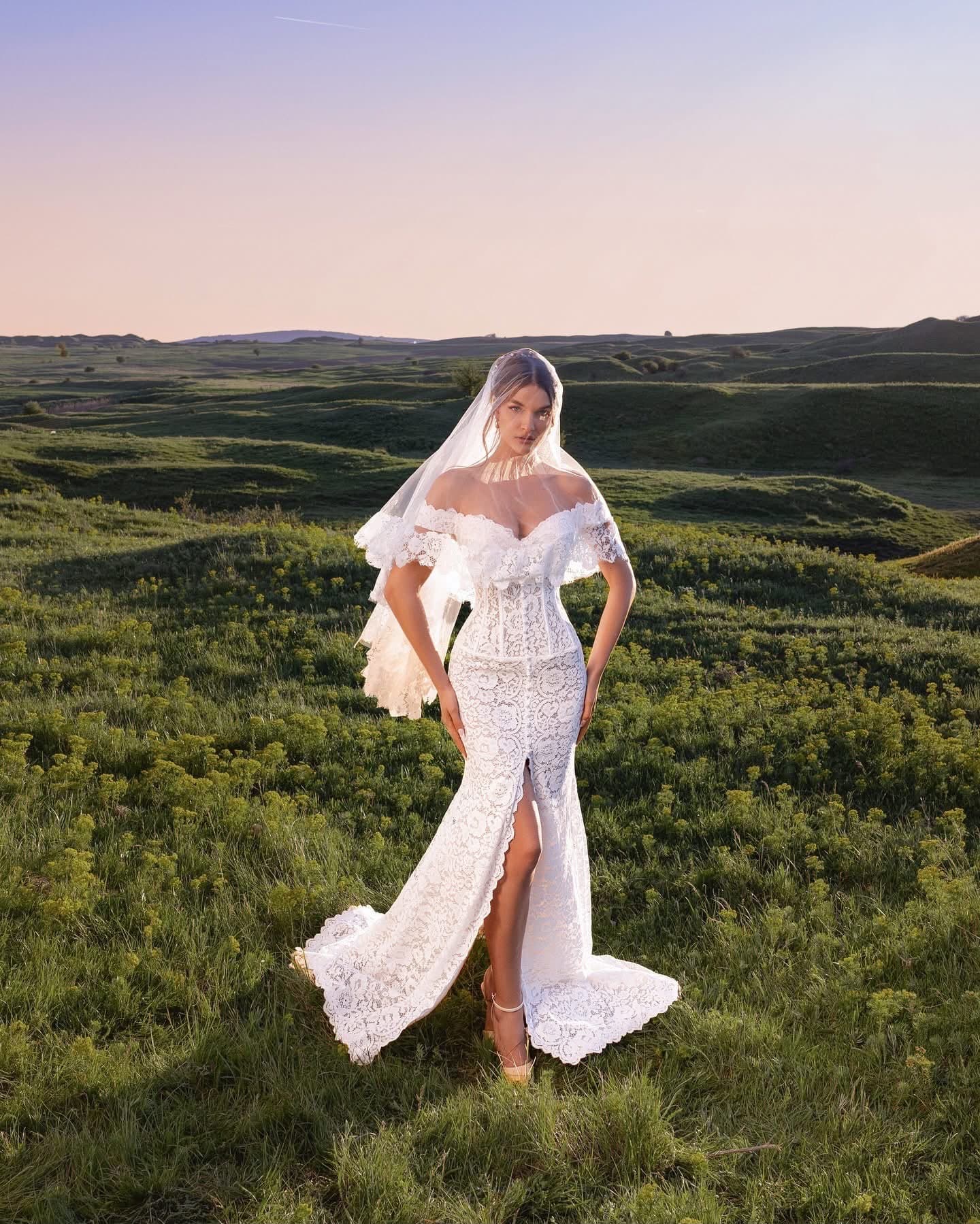 Bride in the Sirène Dentelle lace mermaid gown with veil, full length, on a hillside at dusk