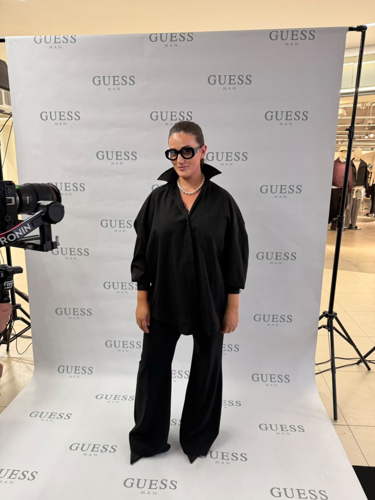 Noir Oversized T-Shirt worn at a press event, styled with wide black trousers and a pearl necklace