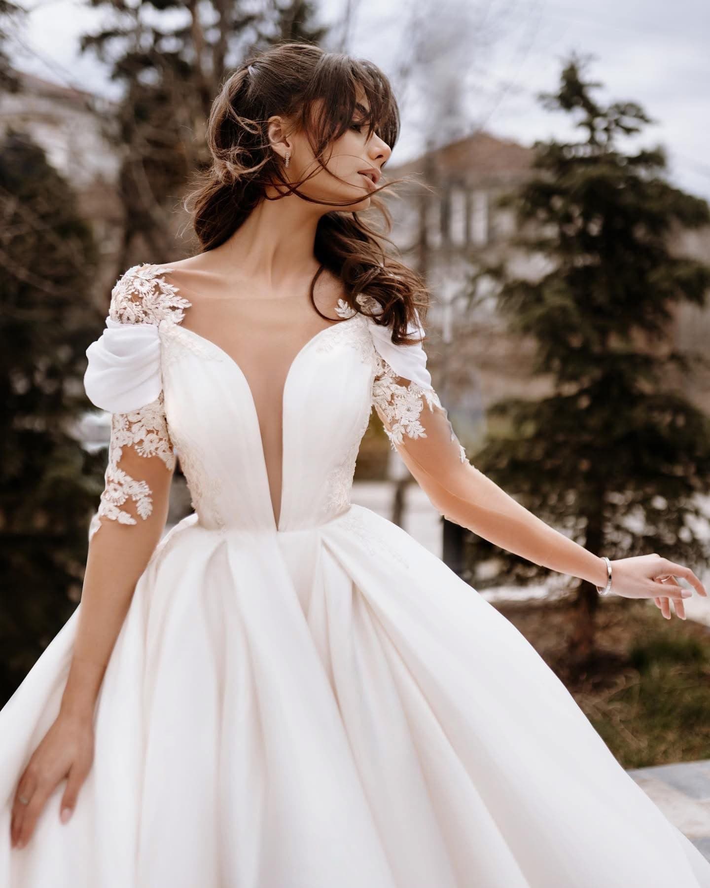 Bride in the Fleur d'Épaule Gown with plunging neckline, lace sleeves and full satin skirt